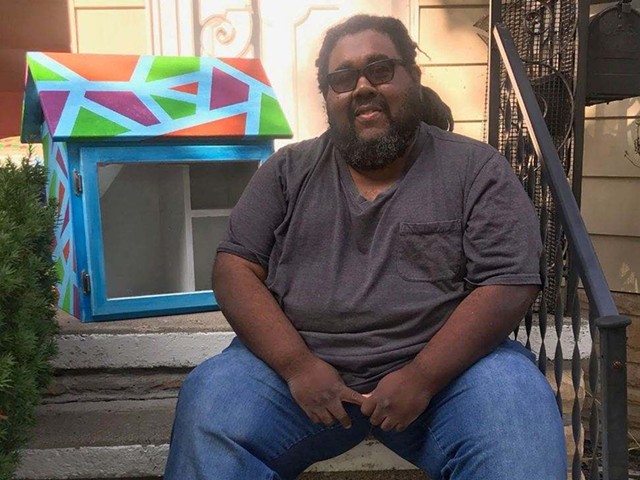 James Chism, Harper Woods resident and participating artist in the Little Library prize, sits with the library he painted, called Breaking Barriers, Smashing Ceilings.