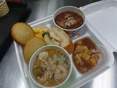 Front, the premium seafood gumbo, Poor Boy sandwich center, cornbread and mac 'n cheese left, peach cobbler right, and red beans and rice back.