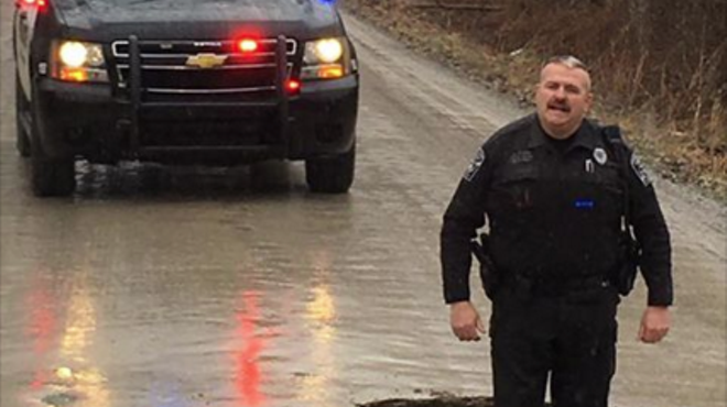 A Grand Blanc Township police officer stands knee-deep in a pot hole on McWain Road.