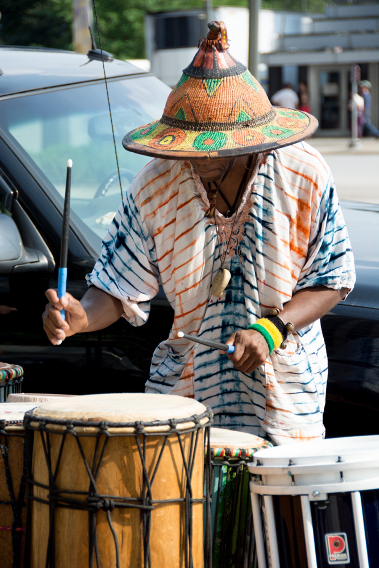 A man with a fantastic beaded hat has some excellent drumming beats.