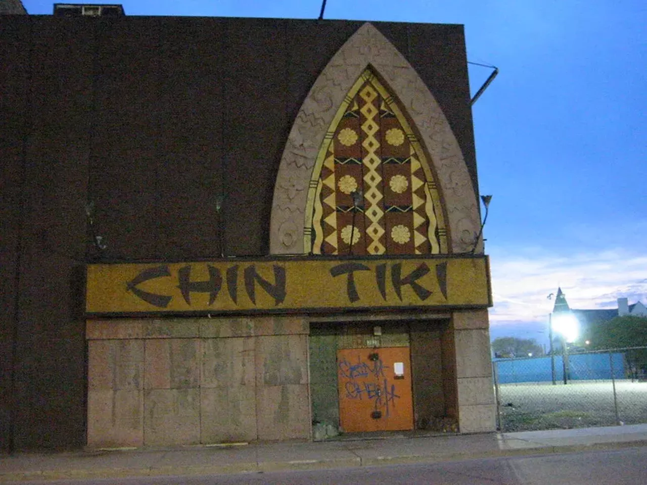 Chin Tiki Detroit currently has a few tiki-themed bars, but before Mutiny Bar in Southwest Detroit and Lost River there was Chin Tiki at 2121 Cass Ave. Established in 1967 by Martin Chin, Chin Tiki was a hotspot in the '60s and reported visits by Muhammad Ali, Barbra Streisand, and Joe DiMaggio. The windowless club featured a lower-level waterfall and bamboo bridge led the way to dozens of romantic, thatch-covered booths, where moony-eyed couples dined on Polynesian delicacies. An enormous aquarium mural glowed under black light, framed a long, elegant rattan bar. The journey upstairs led to an even larger waterfall; the rock-like walls curve around a wave-shaped bar with dozens of Chinese coins suspended in Lucite. The small rattan stage once hosted live music of all genres; an authentic Polynesian floor show, complete with Hawaiian dancers and fire-breathers, was held weekly. When Detroit entered the economic crisis in the 1980s, Chin closed the tiki bar and, aside from being featured in Eminem's autobiographical movie 8 Mile, Chin Tiki remained untouched until it was demolished in 2009. It is now one of many Illitch-owned and sanctioned parking lots. Photo via Jim Rees/Flickr