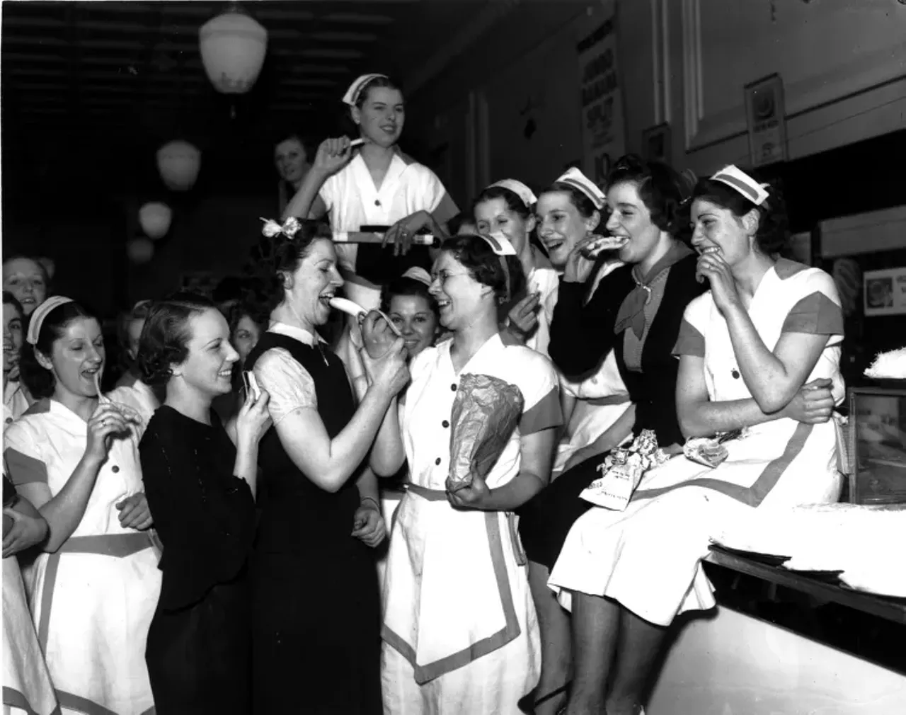 1930s | Striking employees, some in waitress uniforms, pose eating food, during sit-down strike at Woolworth department store in Detroit, Michigan.