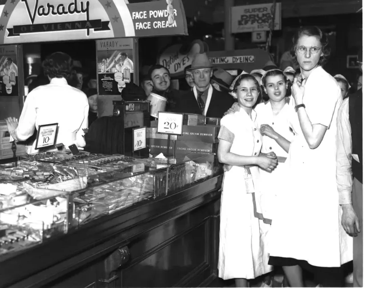 1930s | Women in waitress uniforms stand near make-up counter at Woolworth department store, with men in background, during sit-down strike in Detroit, Michigan.