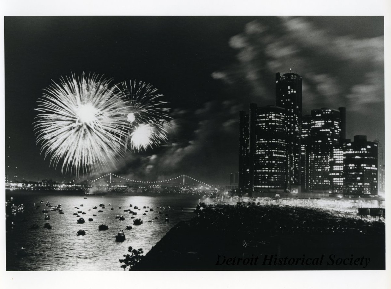"Black and white photographic print depicting a fireworks display over the Detroit River at night, with the Ambassador Bridge to the left and the Renaissance Center to the right. The river is filled with small boats.
Caption reads- Freedom Festival Fireworks - One of the highlights of the 1984 Detroit-Windsor International Freedom Festival was the riverfront fireworks display captured in this photograph by Mark Cornillie. It appeared in newspapers around the country.
An estimated one million people turn out for the show sponsored by Hudson's, Stroh's, WDIV-TV 4 and WMJC-FM.
Handwritten on verso: Used June 1985 Michigan Living"