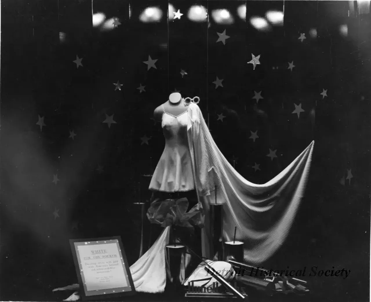 "Print. Black and white photograph of the window display at Himelhoch's Department Store. Fourth of July women's attire is displayed, a short dress with cape, and sunglasses. Signage in the front of the display reads, "WHITE FOR THE FOURTH, Dazzling white with gold — with America's beloved red-white-and-blue accessories! Himelhoch's Fourth Floor, Window No. 2." The date has been noted on the verso, 'June 30, 1940.'""Print. Black and white photograph of the window display at Himelhoch's Department Store. Fourth of July women's attire is displayed, a short dress with cape, and sunglasses. Signage in the front of the display reads, "WHITE FOR THE FOURTH, Dazzling white with gold — with America's beloved red-white-and-blue accessories! Himelhoch's Fourth Floor, Window No. 2." The date has been noted on the verso, 'June 30, 1940.'"