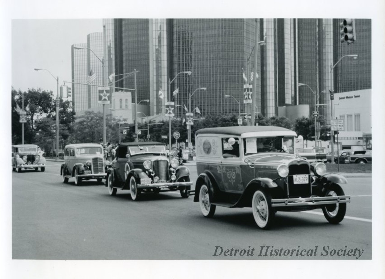"Black and white photographic print depicting a parade of antique cars traveling west on Jefferson Avenue, with the Mariners' Church, Renaissance center, and entrance to the Detroit-Windsor Tunnel in the background.
Caption reads: One of the truly international events of the International Freedom Festival is the Wheels of Freedom Antique Car Display and parade. More than 200 antique, classic and collector cars participate in this event. The day begins with a morning exhibit and judging in Windsor's City Hall Square. The car parade crosses the Ambassador Bridge and ends up in the New center Area for awards ceremonies. Children, adults and senior citizens will gather in New Center to enjoy entertainment of all kinds including music from the '30s through the eighties."