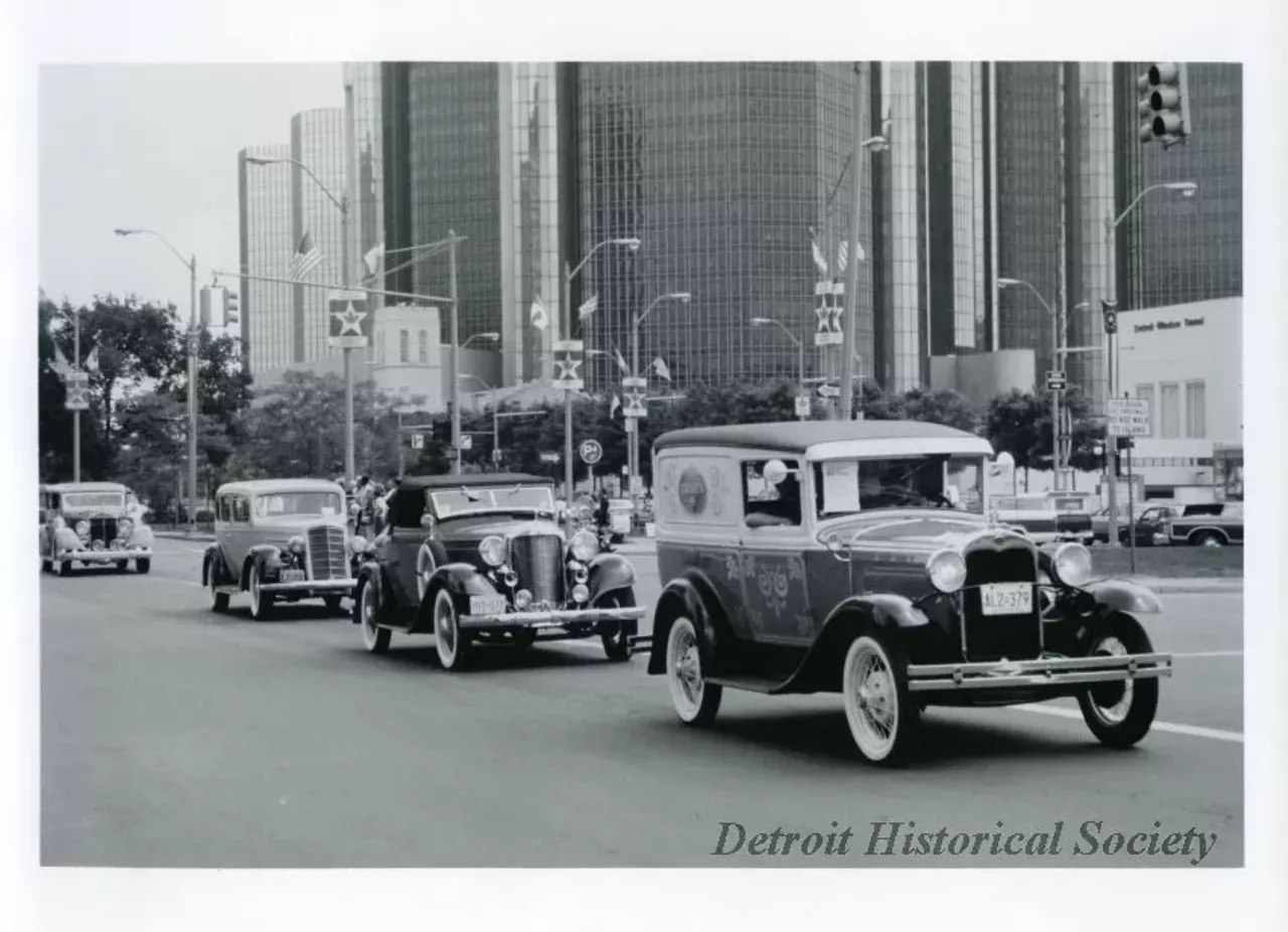 "Black and white photographic print depicting a parade of antique cars traveling west on Jefferson Avenue, with the Mariners' Church, Renaissance center, and entrance to the Detroit-Windsor Tunnel in the background. Caption reads: One of the truly international events of the International Freedom Festival is the Wheels of Freedom Antique Car Display and parade. More than 200 antique, classic and collector cars participate in this event. The day begins with a morning exhibit and judging in Windsor's City Hall Square. The car parade crosses the Ambassador Bridge and ends up in the New center Area for awards ceremonies. Children, adults and senior citizens will gather in New Center to enjoy entertainment of all kinds including music from the '30s through the eighties."