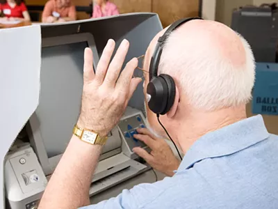 A man uses a touch screen voting machine equipped for the hearing and vision impaired.