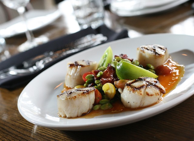 Grilled sea scallops with Swiss chard, tomato, carrot coulis, edamame, bacon lardons and ginger glaze from Detroit Prime.