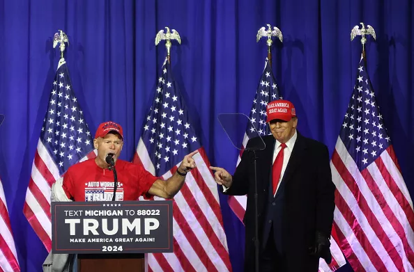 “Look at these muscles”: Former President Donald Trump brings a retired autoworker on stage at a Waterford rally.