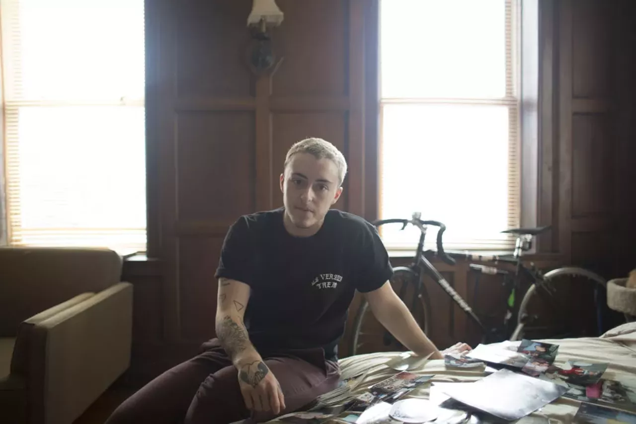 Issa, prior to his top surgery, sitting on his bed with photographs from his childhood.