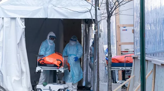 Body of deceased patient in orange bag moved from hospital to refrigerator truck serving as temporary morgue outside of Wyckoff Heights Medical Center in Brooklyn.