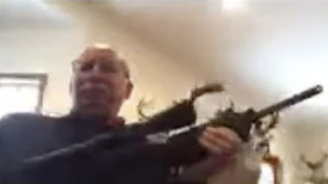 Grand Traverse County Commissioner Ron Clous pulls out a rifle during a virtual public meeting.