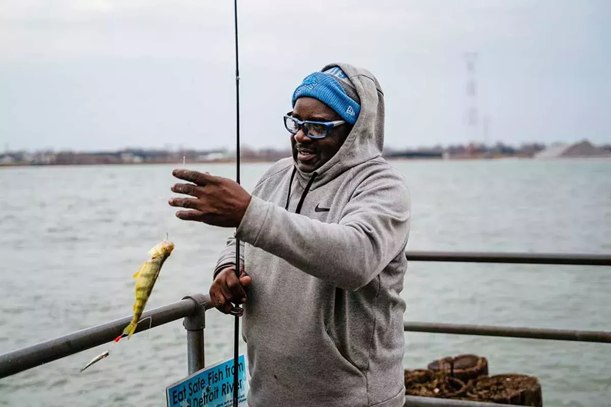 Image: Ivan Bentley unhooks a caught fish and drops it into a bucket at Delray Park.
