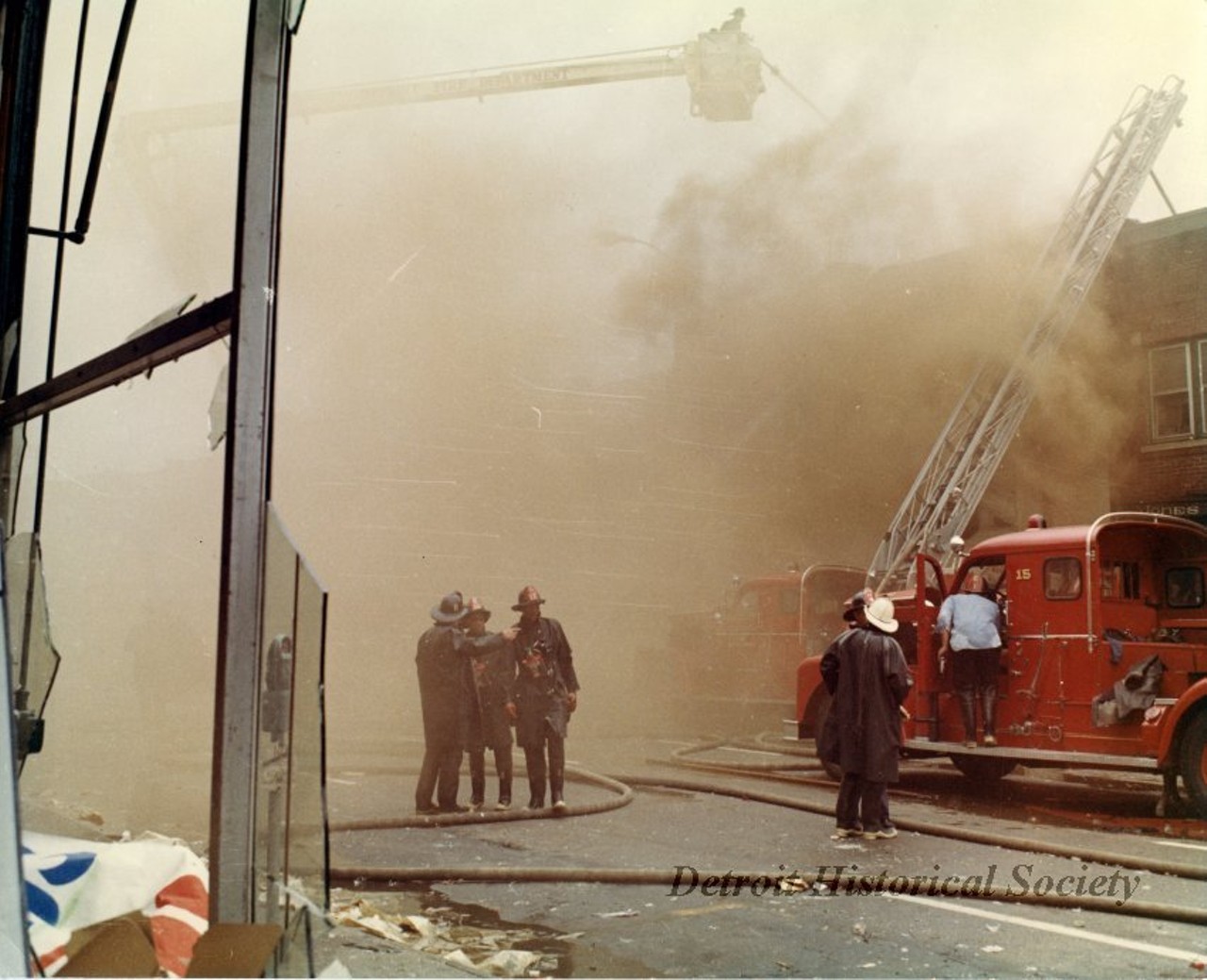 "One color photograph of Detroit firemen who are trying to extinguish a blaze at a row of buildings located on 12th Street between Taylor and Clairmount Streets. The photo shows many fireman at work with aerial and ladder trucks. The buildings had been set on fire during the 1967 Detroit Riot. A red ink stamp on the verso shows 'D.F.D. [Detroit Fire Department] Photo, by Insp. Barney Wasowicz.'"