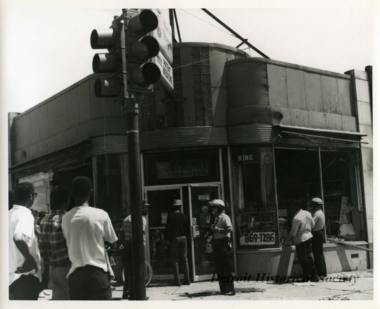 "One black and white photograph of two Detroit Police officers who are on patrol in front of the Golden Bird Patent Medicine store located at 13330 Dexter Boulevard at the corner of Davison Avenue. The two officers are carrying rifles and are wearing helmets. The business was damaged during the recent 1967 Detroit Riot."