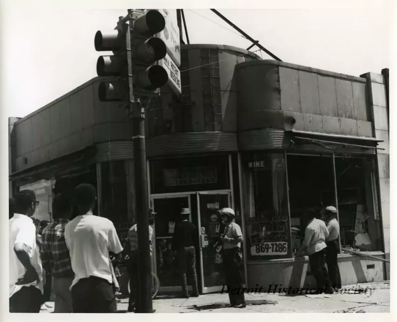 "One black and white photograph of two Detroit Police officers who are on patrol in front of the Golden Bird Patent Medicine store located at 13330 Dexter Boulevard at the corner of Davison Avenue. The two officers are carrying rifles and are wearing helmets. The business was damaged during the recent 1967 Detroit Riot."