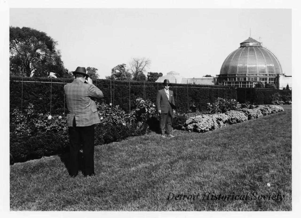 "Black and white photographic print mounted on board depicting a man photographing another in the formal gardens at the Anna Scripps Whitcomb Conservatory. Dated October 1973."