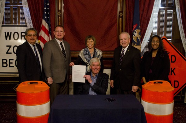 Gov. Rick Snyder signs a supplemental spending bill flanked by orange construction barrels and road work signs. - Courtesy photo