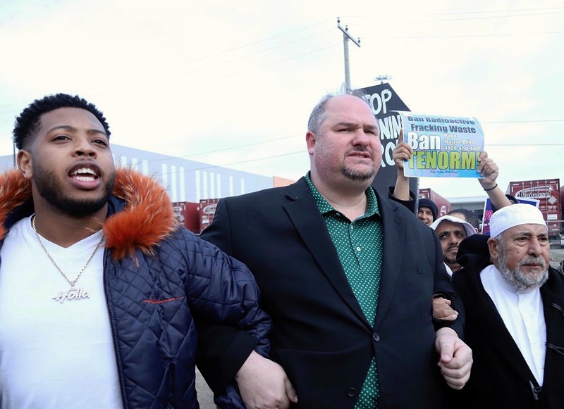 State Rep. Isaac Robinson (center) locks arms with state Rep. Jewell Jones (left) and Imam Salah Algahim (right) as they march from a nearby school to US Ecology on Detroit's east side. - State Rep. Isaac Robinson