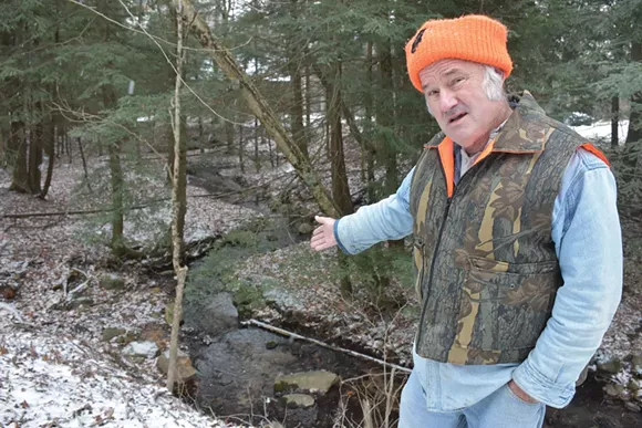 John McLane points to a gentle stream that Nestlé claims flows at 2,058 gallons per minute. - Photo by Michael Jackman.