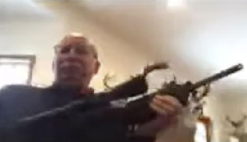 Grand Traverse County Commissioner Ron Clous pulls out a rifle during a virtual public meeting. - YouTube screenshot