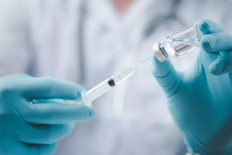 A doctor filling a syringe with a vaccine. - Shutterstock