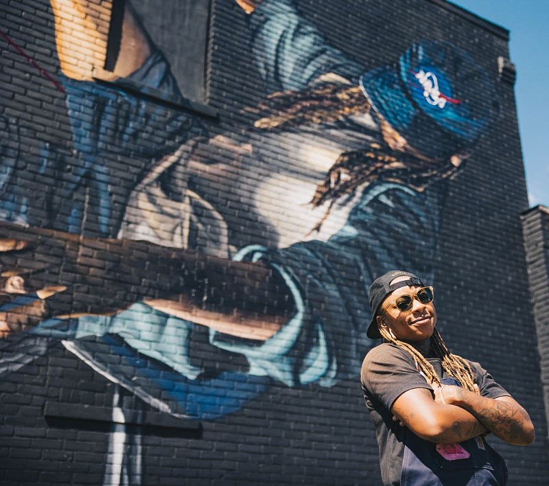 Bakpak Durden poses in front of their mural at BLKOUT Walls Festival. - JUSTIN W. MILHOUSE
