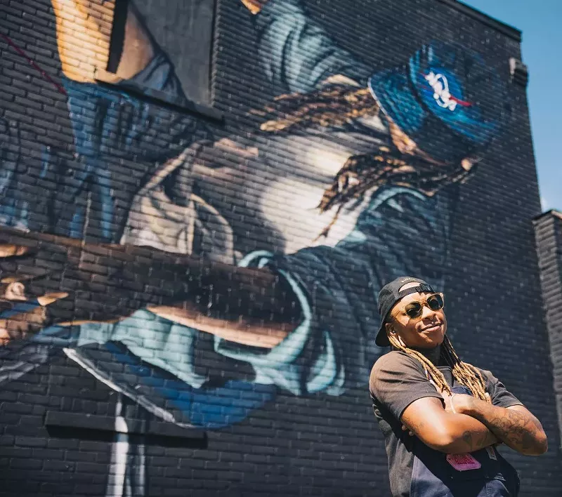 Bakpak Durden poses in front of their mural at BLKOUT Walls Festival. - Justin W. Milhouse