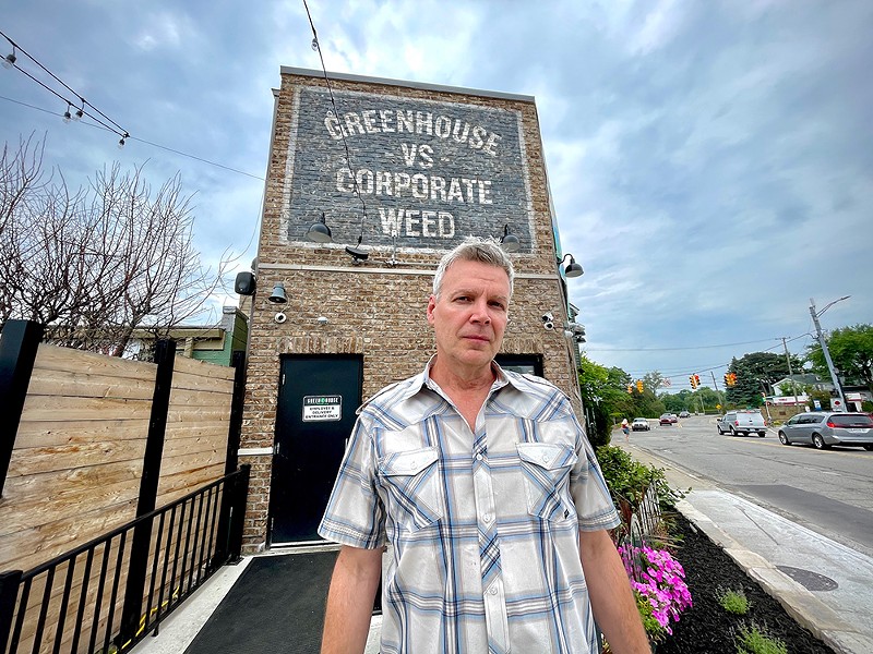 Greenhouse of Walled Lake owner Jerry Millen stands in front of a mural on his dispensary that reads, “Greenhouse vs. Corporate Weed.” - Frank Marra, Greenhouse Of Walled Lake