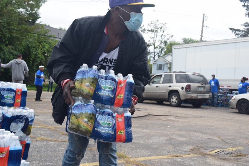 A volunteer carries bottled water to residents waiting to pick it up at God’s Household of Faith Church in Benton Harbor. - Anna Gustafson