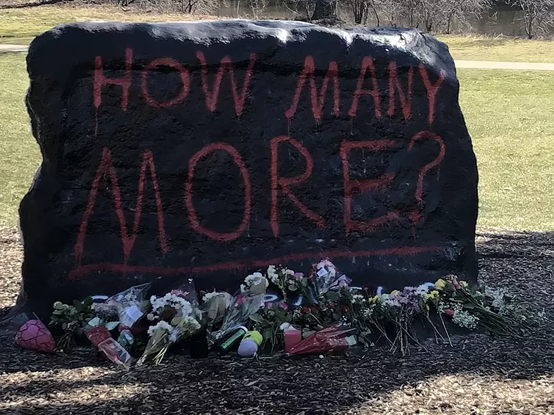 “The Rock” at MSU’s campus has become a memorial to the victims of the Monday shooting, painted with the message “How Many More?” with flowers at its base. - Guettarda, Wikimedia Creative Commons