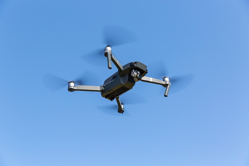 A drone flying against the blue sky. - Shutterstock