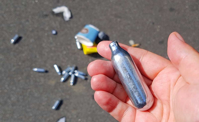 Used cannisters of nitrous oxide litter the ground. - Shutterstock