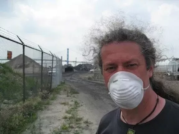 A protester stands in front of the piles of petcoke that graced the riverfront in 2013. The piles are now illegal. - Photo by Curt Guyette