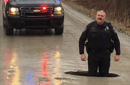 A Grand Blanc Township police officer stands knee-deep in a pot hole on McWain Road. - Facebook, Grand Blanc Township Police Department