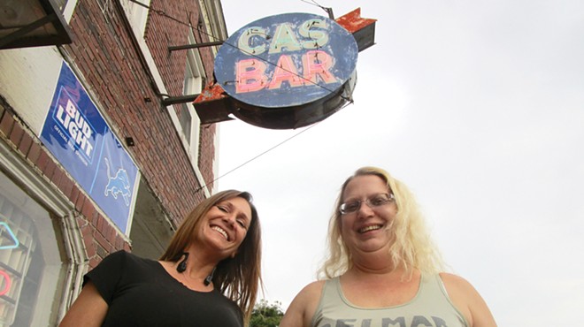 Cas Bar regular Stacie Goolsby and bartender Jodie Welbes pose underneath the bar’s weathered sign.